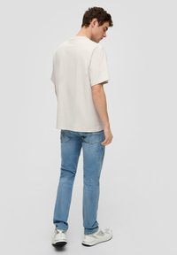 Jasnoszara koszula z krótkim rękawem o luźnym kroju, zestawiona z jasnoniebieskimi dżinsami. Białe trampki z srebrnymi akcentami dopełniają stylizację.