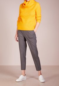 Pull jaune à col roulé en maille, associé à un pantalon gris sur mesure et des baskets blanches. Texture douce et silhouette ajustée.