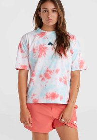 Bílé bavlněné tričko s tie-dye vzorem v růžové a světle modré barvě, krátké rukávy a malá černá grafika u límce. Oblečeno s korálovými šortkami.