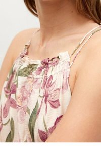 Kwiatowa bluzka bez rękawów z regulowanymi ramiączkami, o kremowej bazie, z fioletowym i zielonym wzorem roślinnym oraz marszczonym dekoltem.