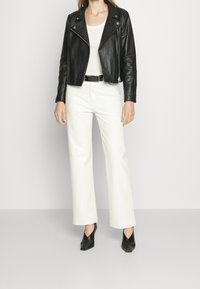 Svart läderbikerjacka med silverfärgad hårdvara, bärs över en vit topp. Matchad med vida vita byxor och svarta klackskor.