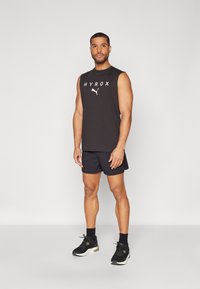 Black sleeveless graphic tank top with "HYROX" text and logo, paired with black shorts and black athletic shoes. Simple design, athletic fit.