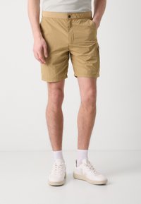 Shorts khaki din material ușor, cu buzunare laterale și o croială lejeră, asortați cu adidași albi și șosete până la gleznă.