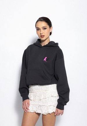 Ciemnoszara bluza z kapturem z różowym logo na klatce piersiowej, z przodu posiada kieszeń oraz miękką, teksturowaną powierzchnię. W zestawie z warstwową białą spódnicą.