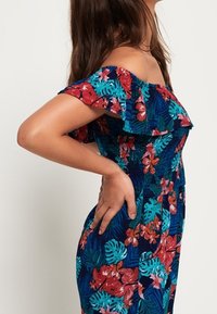 Bloemenjurk met blote schouders, met een marineblauwe achtergrond, levendige roze en turquoise bloemen, een geplooide buste en gerafelde mouwen.