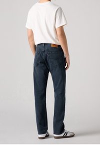 Light blue denim jeans with a straight cut, displaying two back pockets and a brown leather label. Worn with a white t-shirt and sneakers.