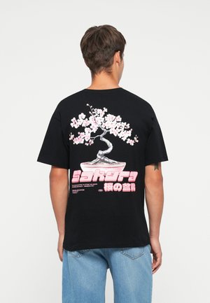 Svart t-skjorte med korte ermer som har et design av rosa kirsebærblomster og stilisert tekst på baksiden, med en avslappet passform og rund hals.