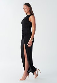 Čierne, bez rukávov, dlhé až po zem šaty s nariasením na boku a vysokým rozparkom na stehne. Hladká látka s priliehavým strihom.