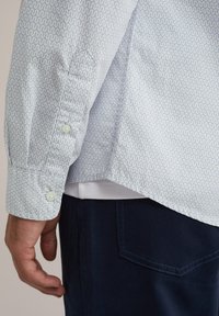 Lichtblauw shirt met een golvend patroon, met knoopmanchetten en kraag. Gecombineerd met donkerblauwe broek met een achterzak.