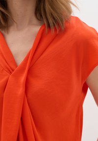 Žiarivo oranžový top s uzlovým dizajnom na dekolte, s krátkymi rukávmi a ľahkým, textúrovaným materiálom.