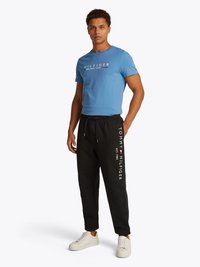 T-shirt di cotone azzurro chiaro con stampa "HILFIGER NEW YORK". Pantaloni joggers neri con logo bianco "TOMMY HILFIGER", vita elastica e sneakers bianche.