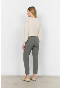 Top beige a maniche lunghe con polsini arricciati, abbinato a pantaloni grigi chiari a gamba affusolata con vita elastica e aperture laterali. Ballerine beige.