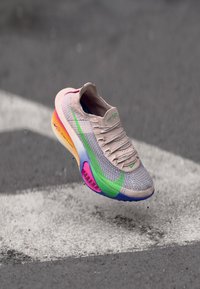 Baskets légères avec un dessus en tricot beige, ornées d'accents verts et bleus, une semelle colorée avec un dégradé allant du rose à l'orange, et une finition texturée.