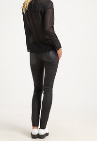 Zwarte doorschijnende blouse met kantdetails bij de halslijn, gecombineerd met strakke zwarte jeans en witte platform schoenen.