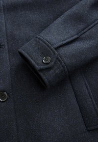 Dunkelblauer Fischgrat-Wollmantel mit einem strukturierten Kragen, Knopfmanschetten und zwei vorderen Taschen, ausgestattet mit schwarzen Knöpfen und strukturiertem Stoff.