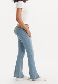 Jeans de campana de color azul claro con un ajuste de altura media, que presentan un parche de cuero en la parte posterior, detalles de costura en los laterales y una textura de denim suave.