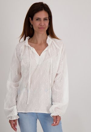 Witte blouse van lichtgewicht stof met zigzagpatroon en opengewerkte details; heeft een geplooide halslijn en elastische manchetten.