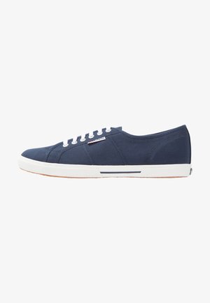 Baskets en toile navy avec des lacets blancs, semelle en caoutchouc et accents rayés. Présente un logo sur le côté et un design basse.