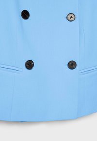 Manteau bleu clair à double boutonnage avec quatre boutons noirs et deux poches horizontales fendues sur la partie inférieure avant.