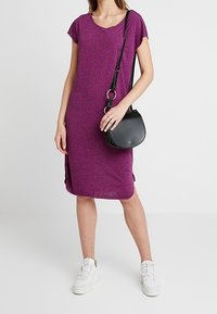 Lila, kortärmad klänning med v-hals, sidofickor, i kombination med en svart axelremsväska och vita sneakers. Tillverkad av ett mjukt, strukturerat tyg.