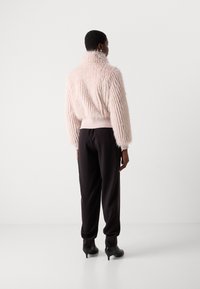 Lichtroze, getextureerde faux bontjas met een hoge kraag, geribbelde zoom en lange mouwen. Gecombineerd met zwarte, op maat gemaakte broek en hoge hakken.