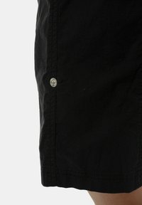 Shorts noirs en tissu léger avec une texture lisse, dotés d'un détail de bouton-pression argenté sur la couture latérale.