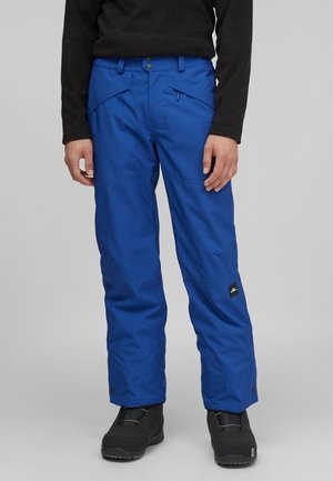 Blaue isolierte Schneehose, getragen mit schwarzen Winterstiefeln und einem schwarzen Langarmtop, von der Taille bis zu den Füßen vor schlichtem Hintergrund gezeigt.
