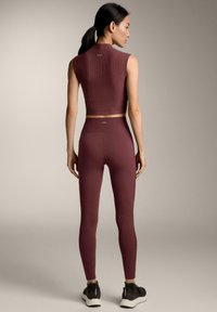 Top corto a coste bordeaux e leggings aderenti, abbinati a sneakers scure. Tessuto liscio, design minimalista e dettagli di branding sottili.