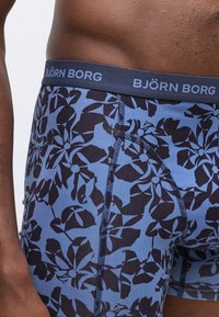 Blue stretch cotton boxer briefs with a black floral pattern. Features a black elastic waistband labeled "BJÖRN BORG." Rounded shape with snug fit.