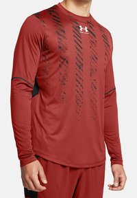 Rotes langärmeliges Sportshirt aus synthetischem Material, mit schwarzen diagonalen Streifen und einem Logo auf der oberen linken Brust.