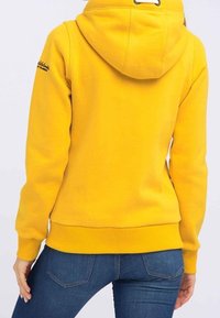 Felpa gialla con cappuccio, polsini e orlo a costine. Presenta un logo sulla spalla sinistra e un tessuto morbido e strutturato.