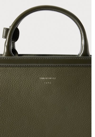 Bolsa de mão de cabedal verde-oliva com superfície texturizada, forma estruturada, duas alças e logotipo discreto em relevo na parte da frente.