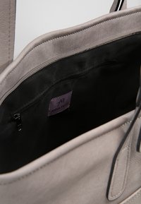 Jasnoszara torba na ramię z miękkim, zamszopodobnym zewnętrzem. Wnętrze z czarnej tkaniny i kieszeń na zamek z metką z logo.