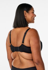 Czarny koronkowy biustonosz z regulowanymi ramiączkami, zapięciem na haftki z tyłu oraz teksturowanym, kwiatowym wzorem na tkaninie.