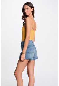 Yellow ribbed bodysuit with thin straps paired with light blue denim shorts. Shorts feature a high waist and two back pockets.