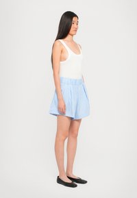 Hvit ribbet tanktopp kombinert med et lys blått og hvitt stripete skjørt med legg, vist på en modell i sorte leiligheter.