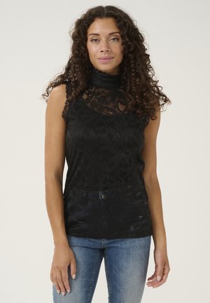 Zwarte kanten mouwloze top met hoge halslijn, voorzien van bloemmotieven en gegolfde randen. Gekoveld met lichtblauwe denim jeans.