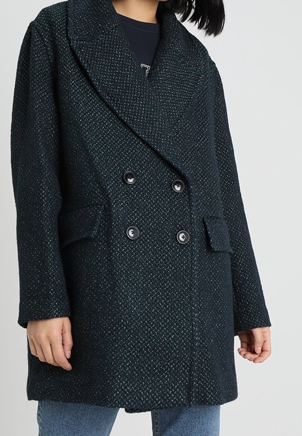 Abrigo de doble botonadura en verde oscuro, fabricado con un tejido texturizado, con grandes solapas, dos bolsillos frontales y detalles de botones negros.
