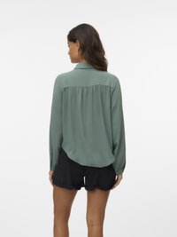 Long-sleeved, mint green blouse with a slightly textured finish, featuring a back yoke and gathered detail, paired with black shorts.
