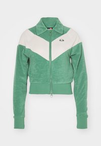 Grön kort jacka i mjuk velour med zipplås framtill, med cremefärgade chevronpaneler och ribbade mudd. Utmärkande logotyp på bröstet.