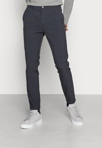 Skräddarsydda grå rutig byxor med smal passform. Har knäppning, fickor och uppvikta fållar. Kombineras med ljusgrå sneakers.