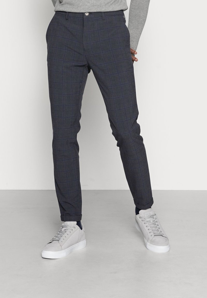 Skräddarsydda grå rutig byxor med smal passform. Har knäppning, fickor och uppvikta fållar. Kombineras med ljusgrå sneakers.