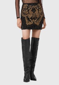 Czarna mini spódnica z cekinami i złotymi ozdobami oraz skomplikowanymi wzorami, w zestawie z dopasowanymi czarnymi kozakami do kolan.