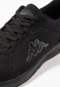 Scarpa sportiva nera, caratterizzata da una tomaia in rete e dettagli in suede. La suola è in gomma, con un logo nero lucido che raffigura due figure.
