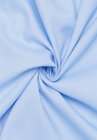 Lichtblauwe geweven stof met een gladde textuur, die een diagonaal patroon vertoont en in een cirkelvormige schuilplaats is gedraaid, wat de flexibiliteit ervan benadrukt.