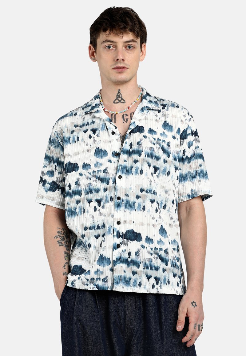 Camicia a maniche corte con bottoni di colore bianco, decorata con motivi tie-dye blu e grigi. Presenta una vestibilità ampia e un colletto, con una finitura in tessuto testurizzato.