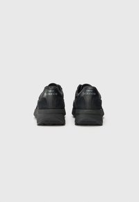 Baskets noires de sport avec un mélange de textures lisses et en daim. Dotées d'une semelle épaisse et du logo "new balance" sur le talon et sur le côté.