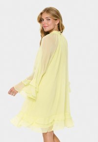 Yellow chiffon dress featuring long, flowing sleeves with ruffle accents, a high neckline, and a tiered ruffle hemline.