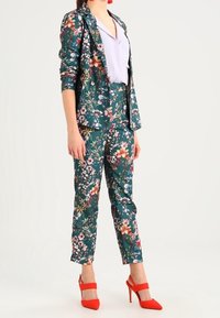 Floral-patterned suit in teal with a fitted blazer and tapered trousers. Accompanied by red high-heeled shoes and a light purple top.
