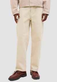 Beige Baumwollhose mit geradem Schnitt und glatter Textur. Kombiniert mit braunen Schnürschuhen aus Leder.